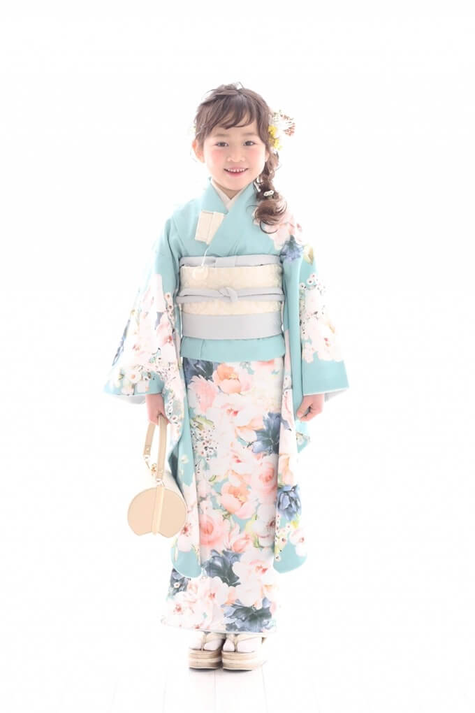 Young girl in a pale blue floral kimono, holding a round bag and smiling for a formal portrait, white background